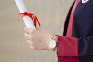 Graduate holding a diploma with a bow tied around it in her hand.